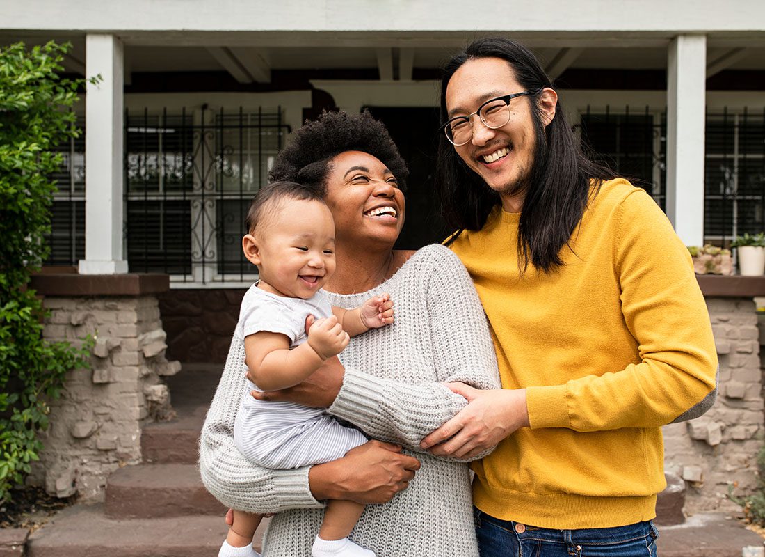 Personal Insurance - Portrait of Excited Diverse Young Parents Holding Their Baby While Standing Outside Their New Home